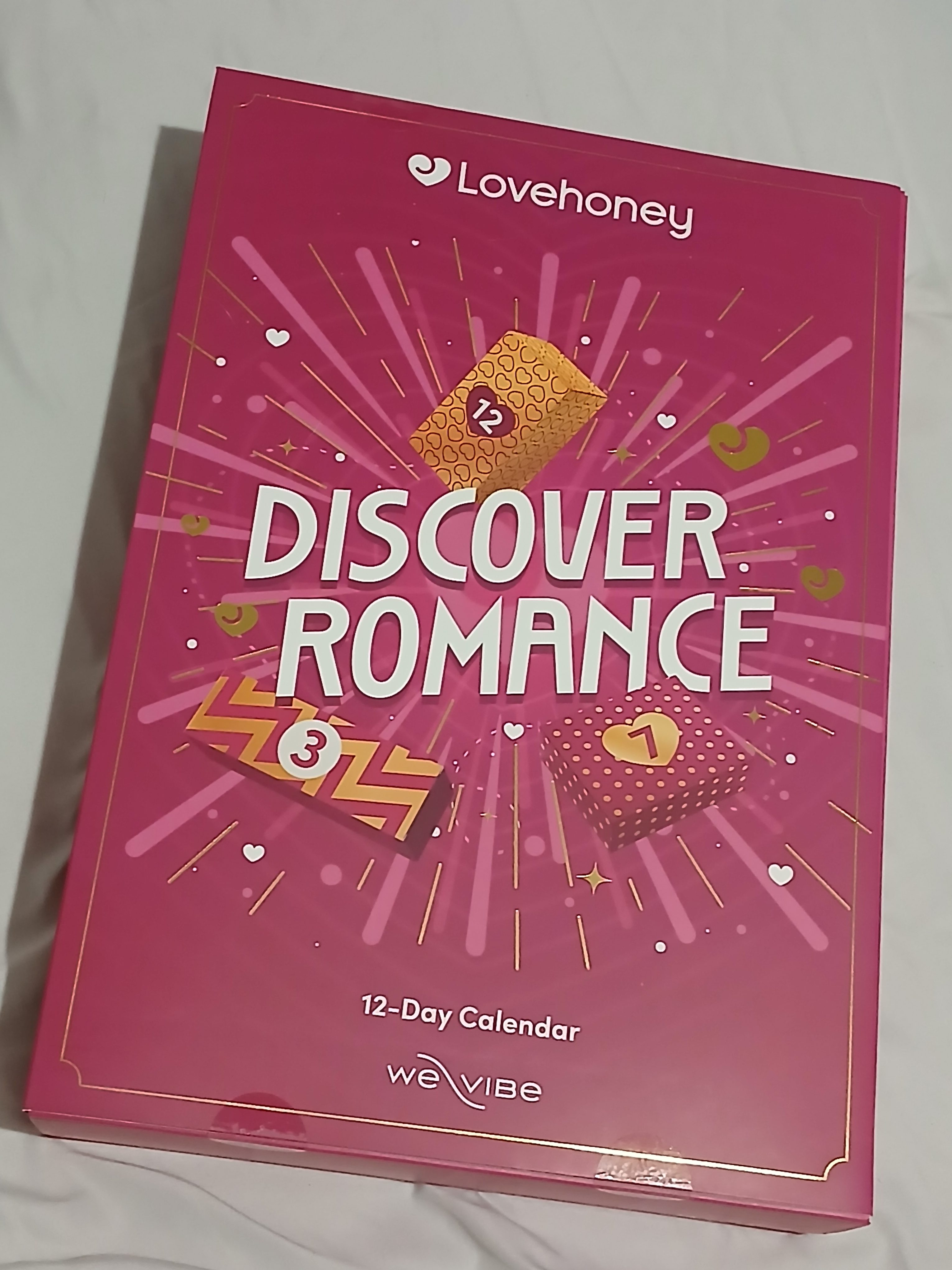 Lovehoney Discover Romance 12 Day advent calendar with We Vibe vibrator on a light folral grey bedspread.