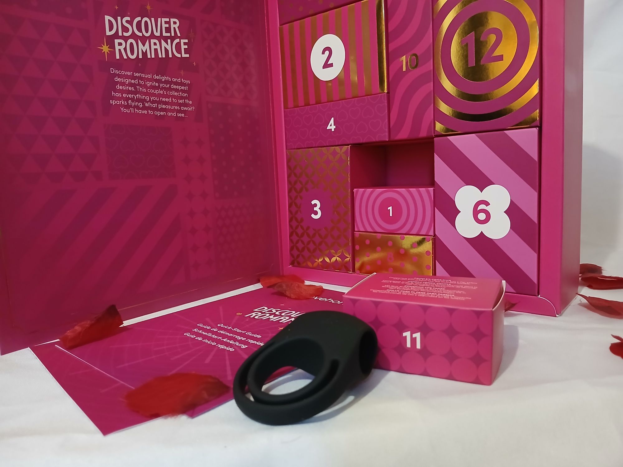 Lovehoney discover romance advent calendar day 11 .A bblack silicone couple's cock ring rests by a pink box with a number 11 on it and a pink advent calendar in the background.